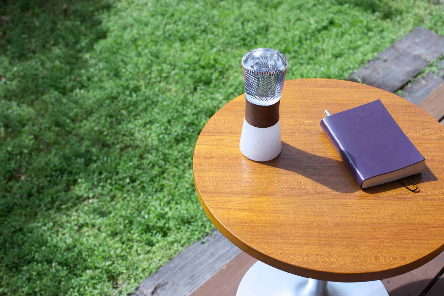 芝生のあるテラスでウッド調の丸テーブル上に紫の表紙の本と置かれたスフェラーランタンの写真