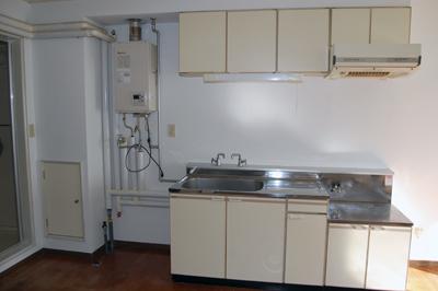キッチンの流し台とガス台、上部に扉付きの棚、左手に給湯ボイラーがある室内写真