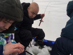 砂川オアシスパーク：つり竿を手に穴を開けた氷の上でワカサギ釣りをする男性の写真